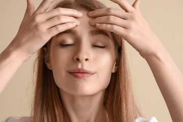 Young woman doing face building exercise on beige background, closeup