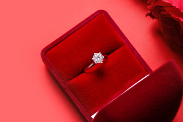 Box with engagement ring and roses on red background, closeup
