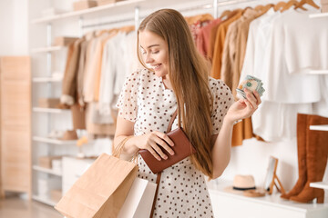 Young woman with wallet, money and shopping bags in boutique