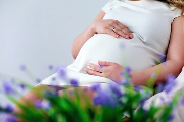 Pregnancy. A pregnant mother in a white dress touches her tummy. Against the background of flowers.