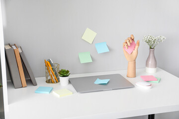 Wooden hand with sticky notes and laptop on table near light wall