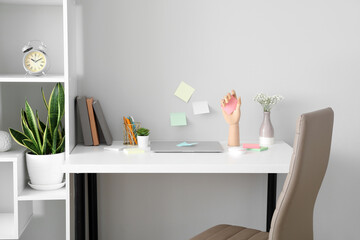 Wooden hand with sticky notes and laptop on table near light wall