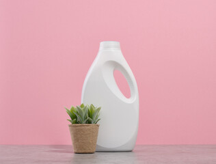 A large white bottle of laundry detergent and a green plant in a pot. Freshness and cleanliness.