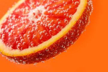 Blood orange slice in water with bubbles on red background