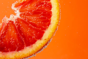 Blood orange slice in water with bubbles on red background