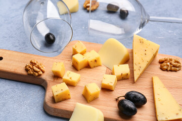 Wooden board with pieces of tasty cheese on grey background, closeup