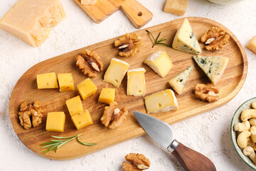 Wooden board with pieces of tasty cheese on light background