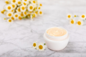Fototapeta na wymiar Body and hand cream with chamomile extract on a marble background. Herbal dermatological cosmetic hygiene cream. Natural beauty product. Cosmetic cream with flowers on wooden background. Spa concept. 