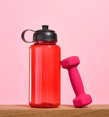 A red sports shaker for drinking clean water during workouts and a pink dumbbell. Exercise workout.
