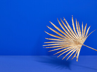 Golden decorative palm branch on a blue background. Copy space for text. Stylish luxury interior.