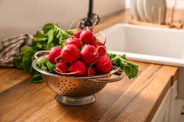Colander with fresh radish on table in kitchen