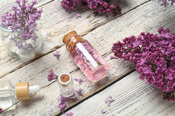 Obraz na płótnie Canvas Composition with bottles of lilac essential oil and flowers on light wooden background, closeup
