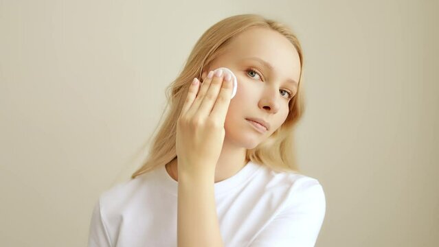 Young woman holding cotton pad disk cleaning face skin with cleanser tonic. Skin care remove make up purify lotion.