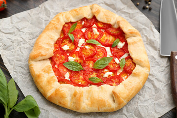 Baking paper with tasty tomato galette and basil on wooden background