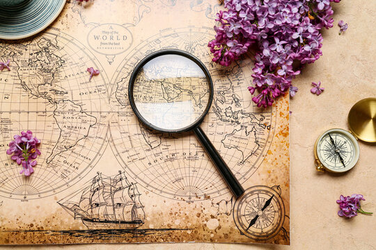 World map with compass, magnifier and lilac flowers on beige grunge background