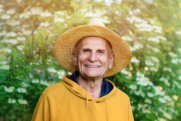 Senior ordinary rustic man wearing strawy hat with smile on wrinkled tanned face on nature background outside