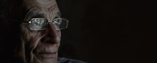 Wrinkled face of senior man wearing glasses on black background. Old lonely male person side view.