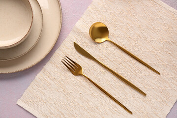 Plates with golden cutlery on lilac background