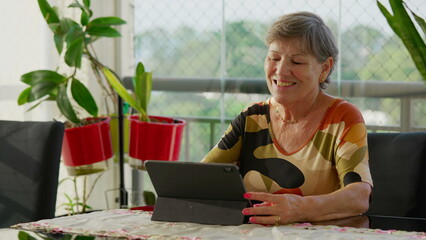 Candid senior woman using tablet at home. Older mature female person looking at modern technology screen with happy expression