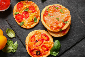 Board with different tasty mini pizzas on black background
