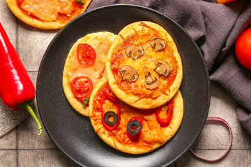 Plate with different tasty mini pizzas on grey tile background