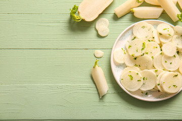 Plate with slices of fresh daikon radish on green wooden background