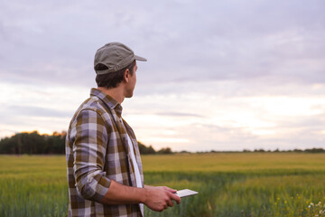 Farmer with a tablet computer in front of a sunset agricultural landscape. Countryside field. The concept of country life, food production, farming and technology concept.