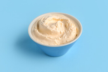 Bowl with tasty cream cheese on blue background