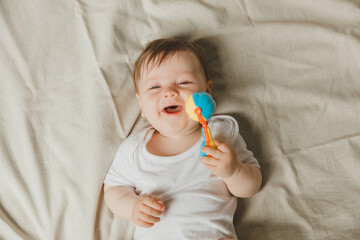 A baby with a teether and a rattle on a cotton bed. Teething. Children's article. copy space