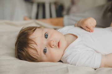 Charming blue-eyed 6-month-old baby lies in bed in a white bodysuit. View from above