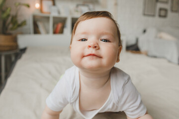 Portrait of a 6 month old crawling baby on the bed. the baby smiles and looks at the camera.