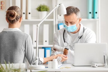 Fototapeta premium Mature male doctor taking patient's pulse in clinic