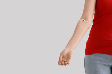 Female blood donor with applied medical patch on light background, closeup