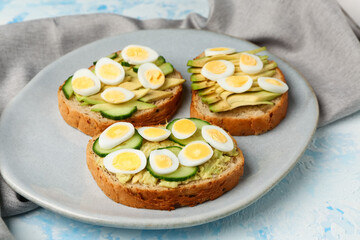 Tasty toasts with quail eggs, avocado and cucumber on light blue background, closeup