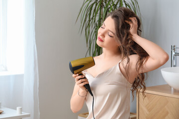 Pretty young woman with hair dryer in bathroom