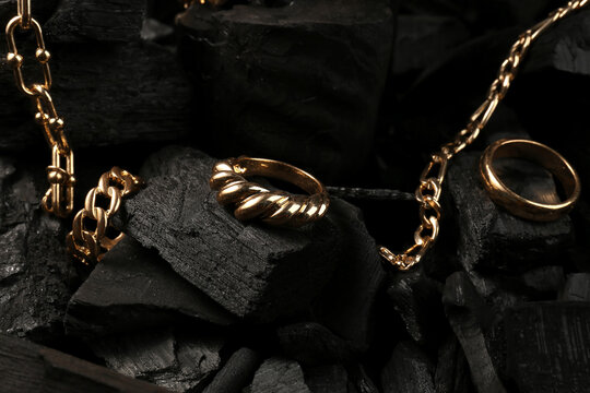 Beautiful chain bracelets and rings on black charcoal, closeup