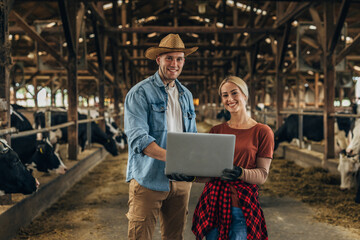 Man and woman holding laptop in a stable and looking at the camera.