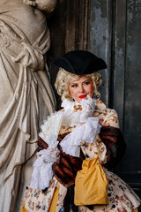 Fototapeta na wymiar Venice, Italy, 11 February 2023: Colorful carnival masks at famous traditional festival on Saint Mark's Square at sunset, Elegant Venetian Costume, historical dress with embroidery and hat with veil