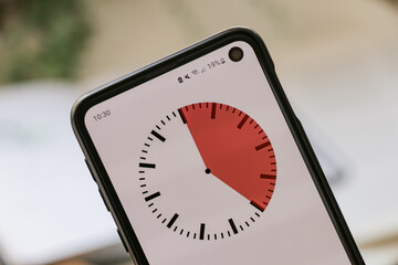 A phone with a red and white 25-minute timer to study with the pomodoro method on a blurry background. Perfect for students planning their time studying, doing homework, being productive.