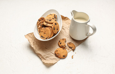 Bowl of cookies and jug with milk on white background