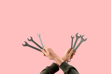 Female hands holding set of wrenches on pink background