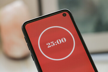A phone with a red and white 25-minute timer to study with the pomodoro method on a blurry background. Perfect for students planning their time studying, doing homework, being productive.