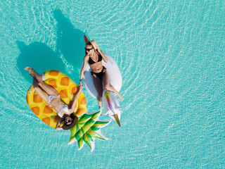 Top view of female friends wearing bikini lying on an inflatable toy in pool. Woman sunbathing on...
