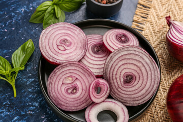 Plate with fresh onion slices and spices on blue background, closeup