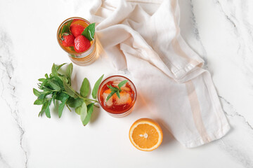 Glasses of ice tea with orange and strawberry on white background