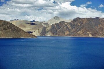 A serene and tranquil scene unfolds as sunlight dances upon the calm waters of Pangong Lake in Ladakh, India.