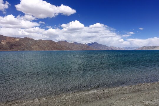 Scenic stock photo of Lake Pangong in Indian Ladakh, bordered by mountains and adorned with clouds.