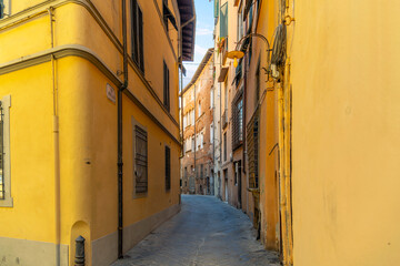 Fototapeta na wymiar A narrow curving alley surrounded by yellow stucco residential buildings in the historic medieval old town of Lucca, Italy, in the Tuscany region.