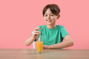 Little boy with glass of orange juice at table on pink background
