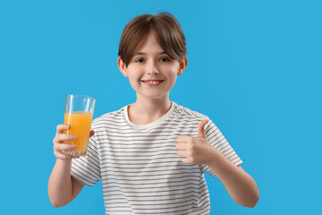 Little boy with glass of orange juice showing thumb-up on blue background